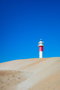 Lighthouse on beach against clear blue sky