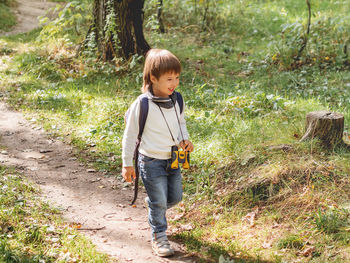 Curious boy is hiking in forest lit by sunlight. outdoor leisure activity. child with binoculars.