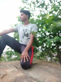 Young man looking away while sitting on tree