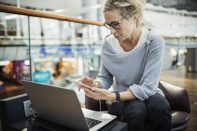 Businesswoman using smart phone and laptop at airport lobby