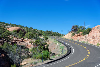 Road leading towards mountains against clear blue sky