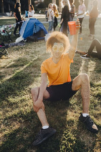 Portrait of man enjoying drink while sitting on grass during music festival