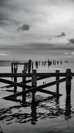 Wooden posts in sea against sky