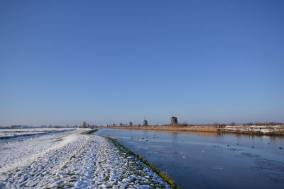 Traditional windmills by river against clear sky during winter