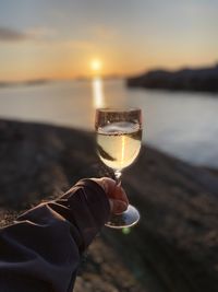 Close-up of hand holding glass of wine at sunset