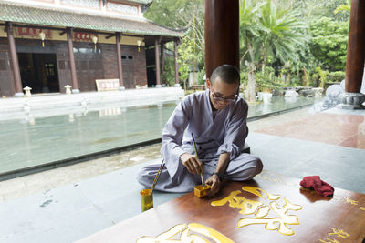 Happy young monk in temple painting on a board