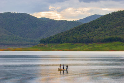 Scenic view of people fishing at lake against mountains and sky