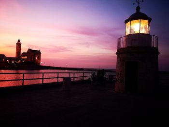 View of lighthouse by building against sky during sunset