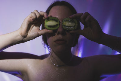 Young woman covering eyes with kiwi fruits