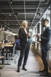 Senior businesswoman discussing with male coworker while standing in office