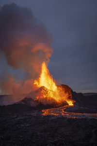 Splashes of hot orange lava erupting from volcanic mountain peak surrounded with smoke in iceland