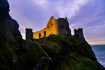 Low angle view of dunluce castle on mountain against sky