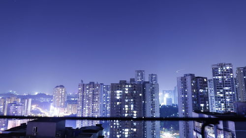 Illuminated buildings against clear blue sky at night