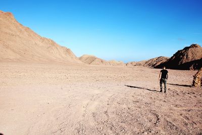 Rear view of man walking at desert against blue sky