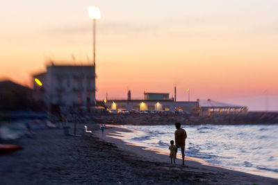 Rear view of silhouette father with son walking on beach during sunset