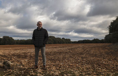 Adult man in winter clothes in fields against cloudy sky
