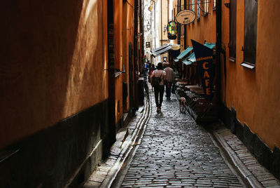 Rear view of people walking on footpath amidst buildings