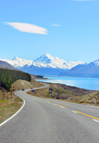 Road by snowcapped mountains against blue sky