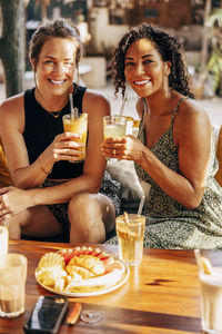 Portrait of smiling female friends enjoying healthy drinks while sitting at wellness resort