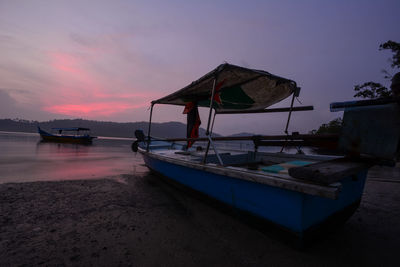 Boat moored on beach against sky during sunset