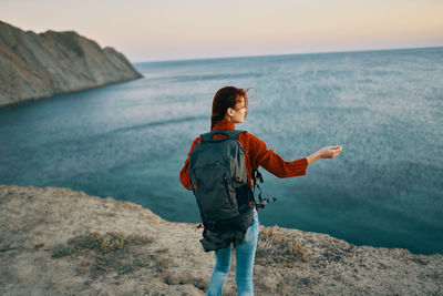 Man standing on rock looking at sea shore against sky