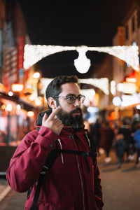 Thoughtful man pointing while standing in city at night