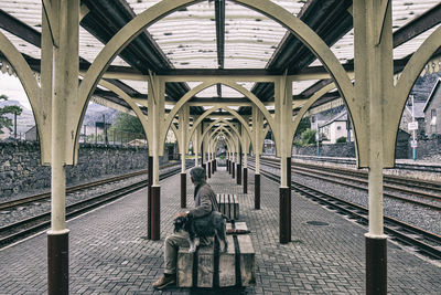 Man sitting with dog on seat at railroad station platform