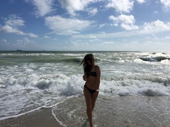 Woman wearing bikini while wading in sea against sky