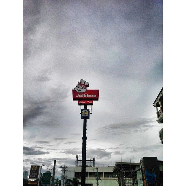 transfer print, sky, low angle view, guidance, building exterior, road sign, built structure, text, communication, architecture, cloud - sky, western script, auto post production filter, pole, information sign, flag, sign, street light, cloudy, cloud