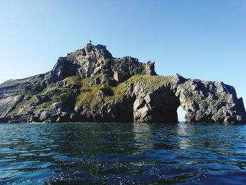 Rock formations by sea against clear blue sky