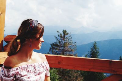 Smiling woman by railing against mountains and sky
