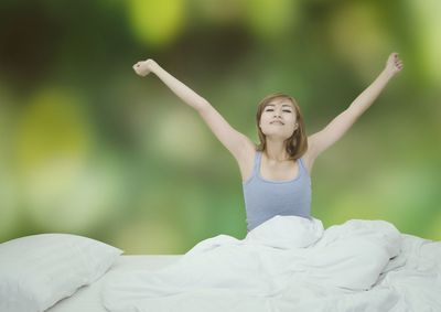 Woman stretching hands on bed against trees