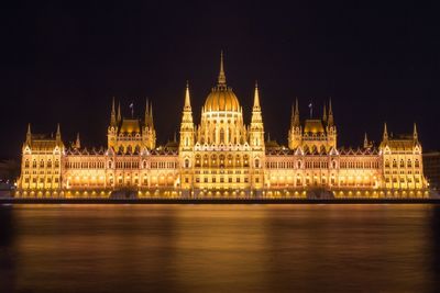 Illuminated hungarian parliament building by danube river against sky at night