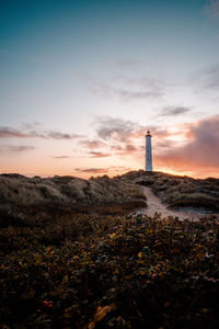 Lighthouse on field against sky during sunset