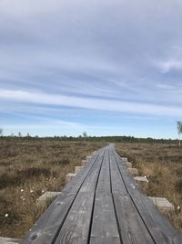 Dirt road amidst field against sky