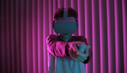 Boy wearing virtual reality simulators while standing against wall