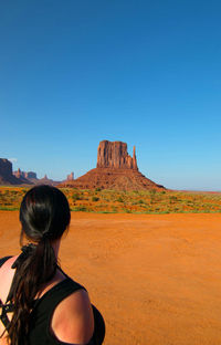 Rear view of woman on rock formations against clear blue sky