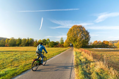 Man riding bicycle on road amidst field against sky