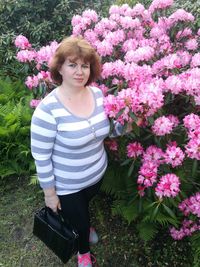 Portrait of woman standing by pink flowering plants at park