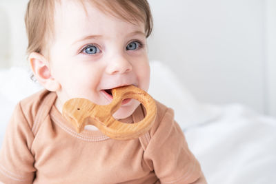 Portrait of baby girl with blue eyes plays with wooden toy teether for teeth on white background