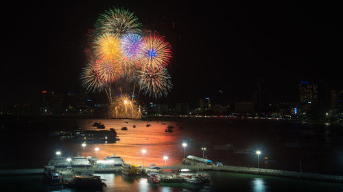 Firework display over illuminated city against sky at night