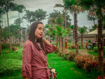 Beautiful young woman standing by palm trees