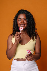 Portrait of smiling young woman eating food against yellow background