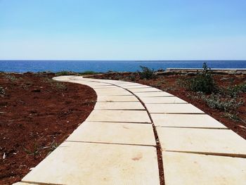 Footpath by sea against clear sky