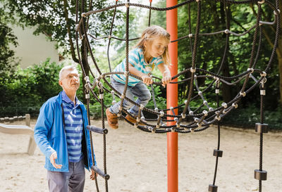 Grandfather standing by daughter playing in playground