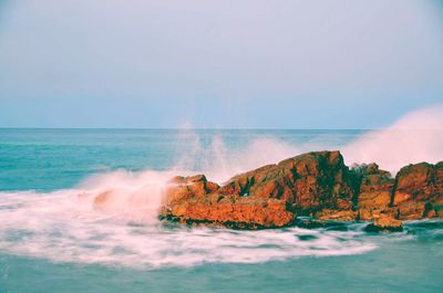 Scenic view of waves crashing on rocks against sky