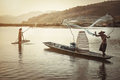 Man standing on fishing boat in lake against sky