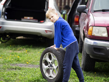 Side view portrait of boy standing with tire on land