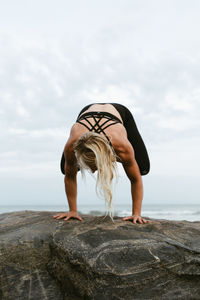 Woman standing on rock by sea against sky