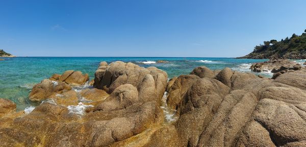 Panoramic shot of rocks on beach against clear blue sky